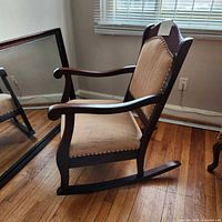 Side angle view of wooden rocking chair showing tan corduroy upholstery on seat and backrest, wood frame and armrests, floor reflection in mirror.