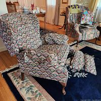 Wingback recliner chair shown in reclined position with footrest extended. Fabric features multicolor fan-shaped pattern. Wooden feet are curved and carved.