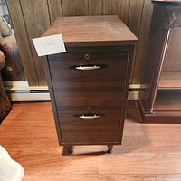 Front view of the dark wood file cabinet showing two drawers with metal handles and slight wear on the surface.