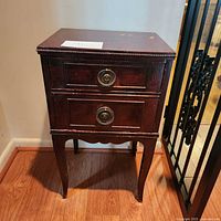 Front view of wooden Federal style nightstand showing two drawers with large round metal pulls and tapered legs.