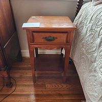 Side view of vintage wooden side table with one drawer, metal handle, scalloped edge below drawer, and lower shelf.
