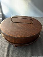 Closed view of the round oak wooden box with carrying handle on top.