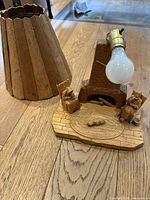 Photo showing wooden lampshade and lamp base with light bulb socket and attached light bulb lying on wooden floor