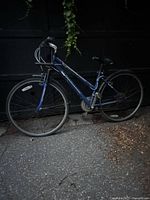 Blue hybrid bicycle parked on asphalt in front of a dark door, shown in dim light conditions; visible wear and no key for lock.