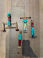 Four colorful carved wooden folk art figures arranged on a wooden floor with visible grain.