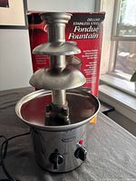 Photo showing the Betty Crocker Deluxe Stainless Steel Fondue Fountain with its original red box in the background.