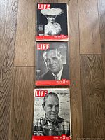 Three vintage LIFE magazines stacked vertically on a wood floor. Covers show black-and-white portraits of individuals from mid-20th century.