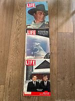 Three LIFE magazines placed on wooden floor showing front covers.