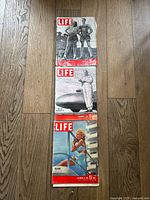 Three vintage Life magazines from 1947 placed vertically on a wooden floor, showing front covers with color and black-and-white images.