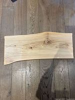 Top-down view of a maple wood plank charcuterie board with natural wood grain, placed on a wooden floor.