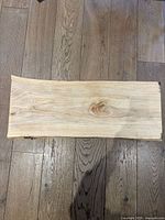 Top view of a rectangular maple wood charcuterie board showing natural wood grain and knots, lying flat on wood flooring.