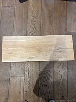 Top view of rectangular maple wood charcuterie board laid flat on wooden floor, showcasing natural wood grain and coloration.