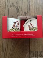 Red display box with clear plastic front showing a fine bone china mug and matching coaster featuring guinea pig and greenery artwork by Hannah Dale.