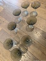 Set of 8 smoky grey martini glasses shown from above on wooden floor, arranged in a circle.
