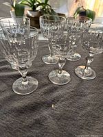 Photo showing six clear stemware glasses with geometric cut pattern, arranged on a table with natural light.