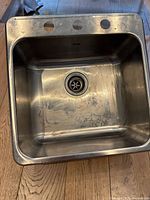Photo showing top view of a stainless steel kitchen sink with four holes for faucet installation and visible interior surface marks.
