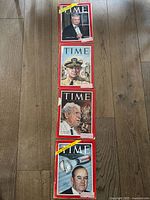 Four TIME magazines arranged vertically on wooden floor showing front covers dated 1958 with illustrations of prominent figures of that time behind red border frames.