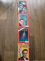Four TIME magazines laid out flat on wooden floor, showing covers as described.