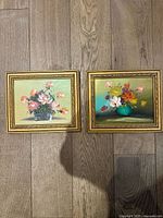 Two vintage floral oil paintings side by side with gold frames on floor