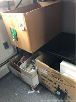 Boxes containing multiple bags and items of costume jewelry, some labeled golf bracelets and sports puzzle pins, wooden bracelets, and other assorted pieces. Large cardboard boxes also include other miscellaneous items such as Beanie Babies and Christmas decor items.