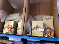 Two Pooh and Friends figurines in original boxes shown from above in cardboard box, includes Pooh Bear with Piglet and Pooh Bear rocking horse figurines.