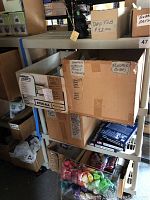 Storage shelving with multiple labeled cardboard boxes containing small items including rubber bands and 'Floced Bears'