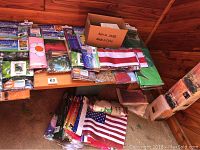 Overview photo showing multiple decorative flags in original packaging on a wooden surface, including an American flag and various floral designs.