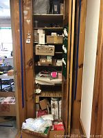 Closet space filled with shelves holding numerous boxes, predominantly cardboard, many labeled fragile or with product codes, with items stacked on the floor beneath the shelves, some folded fabric or soft items visible.