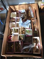 Overview of box containing multiple small white and pink boxes with gold-tone bird and cross ornaments and other decorations, some with crystals.