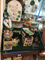Photo showing Irish-themed decorations including leprechaun dolls, shamrock plaques, snow globes, candle melter box, and mantel clock.