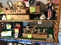 Shelving display of patriotic nutcracker, gold mask, star ornaments, porcelain trinket box, and other collectibles.