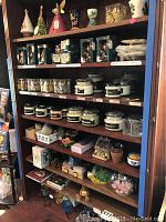 Full view of wooden shelving with assorted candle holders, boxed ornaments, Beanpod candles and decorative items