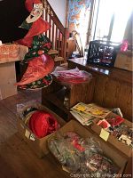 Wide view showing Santa fabric spinner hanging, cardboard boxes with various pins and crafts, lighthouse art prints stacked on a chair.