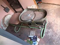 Overview photo showing the full potters wheel including round wheel head, attached metal frame and seat, displaying wear, surface rust, and dirt.