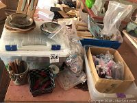 Wide view of assorted bowls, plates, plastic bin, and jewelry-making materials on table.