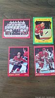 Front of 4 1973 OPC hockey cards showing New York Rangers team card, Dennis Hull All-Star West card, Jacques Lemaire Canadiens card, and Bob Leiter Flames card on wood surface.
