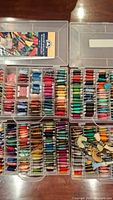 Four clear plastic cases showing multiple rows of embroidery thread bobbins in a variety of colors arranged inside the cases.