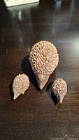 Three wooden hedgehog figurines on a dark wood surface, showing the size difference between adult and babies.