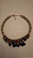 Frontal photo showing entire colorful woven fabric tassel necklace laid flat on surface.