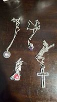 Photo showing four necklaces including a round pendant with clear stones, a small purple stone pendant, a red stone pendant, and a cross pendant.