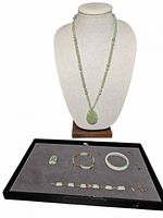 Front view of necklace displayed on bust with jade bracelets laid below on tray.