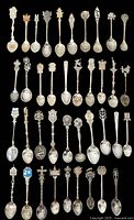 Top view of all 39 souvenir spoons arranged in rows on a black background showing detailed handles and bowls.