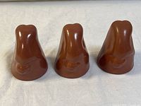 Front view of three brown ceramic abstract sculptures arranged in a row on white fabric background, showing smooth forms and carved details