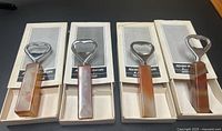 Four vintage bottle openers in original boxes arranged in a row, showing their rectangular stone handles and metal tops.
