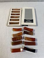 Twelve agate chopstick rests laid out next to the original box showing each rest and their color variations.