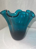 Teal art glass vase showing thickness of glass and ruffled rim on a neutral background