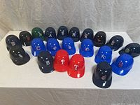 Full display of twenty-one mini MLB souvenir baseball helmets arranged on white fabric background, showing various team logos and colors.