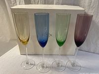 Set of four Lenox crystal champagne flutes in front of Lenox branded box showing all colors: gold, blue, green, purple.