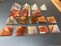 Top-down view of 16 polished agate stone pyramids arranged in rows showing a variety of natural banded patterns and earthy tones from creamy whites to rich carnelian reds.
