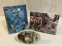 Three wildlife art items: two rectangular prints featuring wolves and moose, one oval plate with wolf portrait